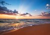 Sunset over a beach with waves and clouds.