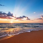 Sunset over a beach with waves and clouds.