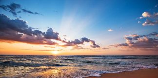 Sunset over a beach with waves and clouds.