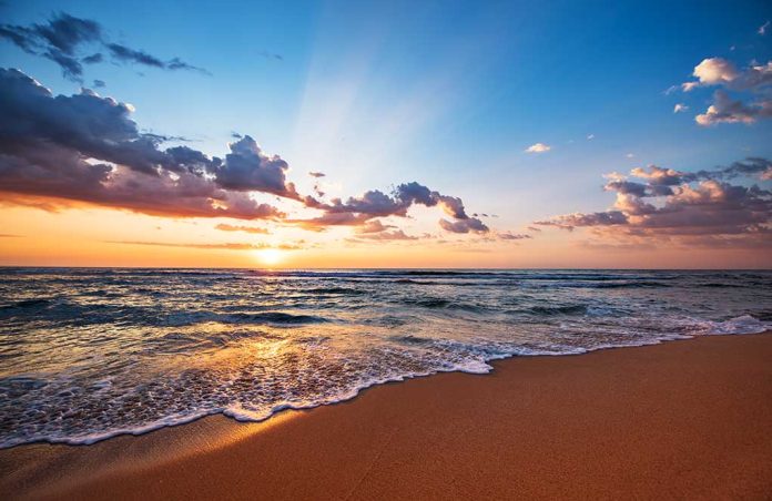 Sunset over a beach with waves and clouds.