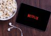 Popcorn, tablet displaying Netflix, and earphones on table.