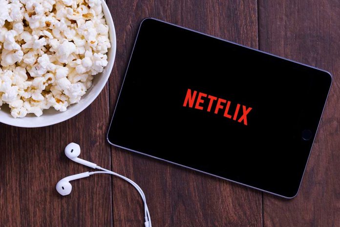 Popcorn, tablet displaying Netflix, and earphones on table.