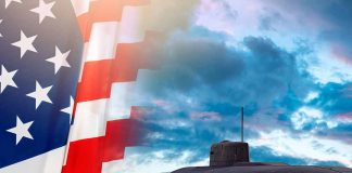 American flag and submarine at sea under a cloudy sky.