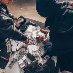 Two individuals handling stacks of money on a table.