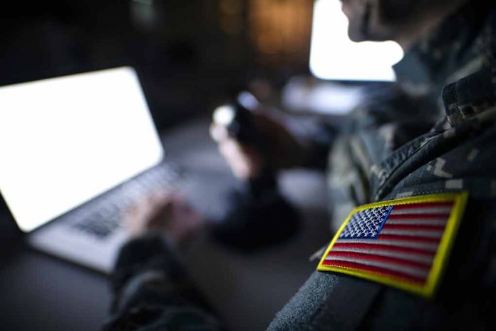 Soldier using laptop with US flag patch visible.