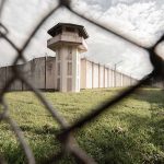 Prison watchtower and fence viewed through chain-link fence.