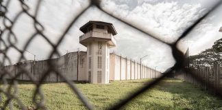 Prison watchtower and fence viewed through chain-link fence.