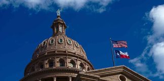 Building dome with US and Texas flags, blue sky.