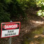 Sign above a ditch reading Danger: Raw Sewage