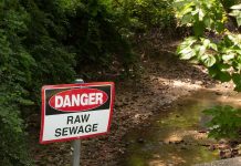 Sign above a ditch reading Danger: Raw Sewage