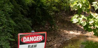 Sign above a ditch reading Danger: Raw Sewage