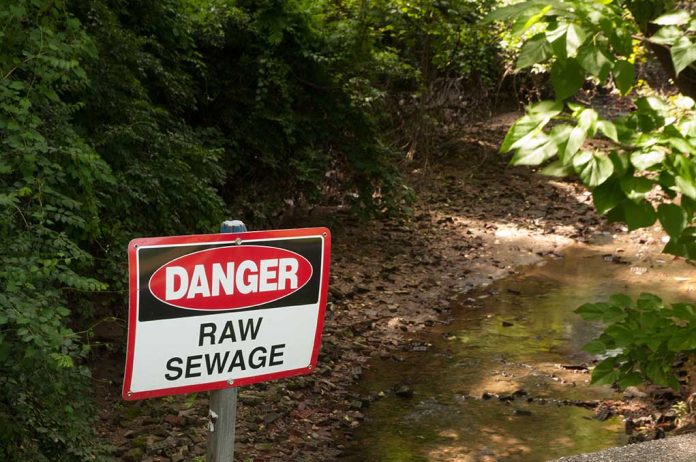 Sign above a ditch reading Danger: Raw Sewage