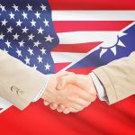 Two people shaking hands with USA, Taiwan flags.