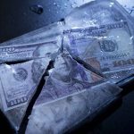 Hundred-dollar bills frozen in cracked ice block.