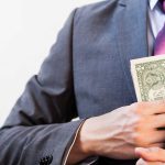 Person in suit putting money in jacket pocket.