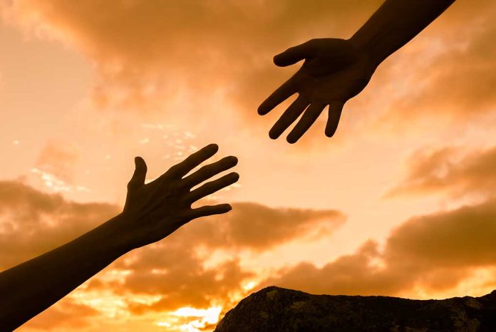 Two hands reaching against a sunset background.