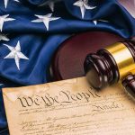 Gavel on U.S. Constitution with American flag background.