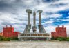 Concrete monument with hands holding tools under cloudy sky.