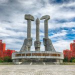 Concrete monument with hands holding tools under cloudy sky.