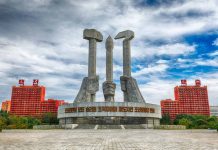 Concrete monument with hands holding tools under cloudy sky.