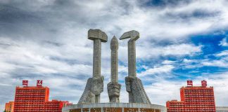 Concrete monument with hands holding tools under cloudy sky.