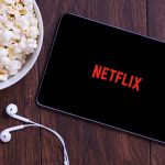 Popcorn, tablet displaying Netflix, and earphones on table.