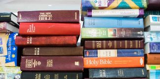 Several Bible editions stacked on a bookshelf.