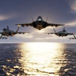 Five jets flying low over the ocean at sunset.