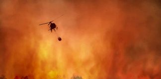 Helicopter fighting massive forest fire with water bucket.