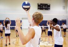 Players about to serve a volleyball in gym.