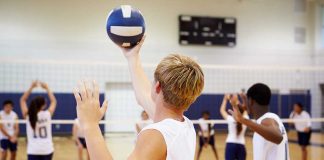 Players about to serve a volleyball in gym.