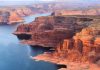 Red rock canyons beside blue water body.