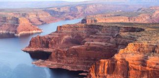 Red rock canyons beside blue water body.