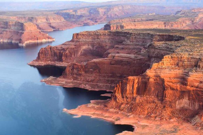 Red rock canyons beside blue water body.