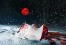 Red moon above snowy tent in blizzard night