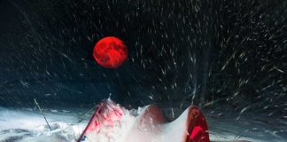 Red moon above snowy tent in blizzard night