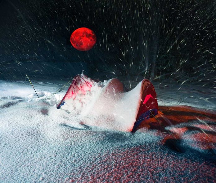 Red moon above snowy tent in blizzard night