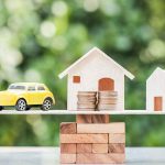 Toy car and houses balanced on stacked coins.