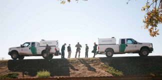 Border patrol agents near vehicles on embankment daytime