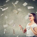 Woman holding phone surrounded by falling money