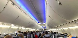 Airplane cabin with passengers and in-flight entertainment screens.