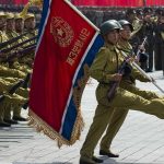 Soldiers marching with flag in military parade.