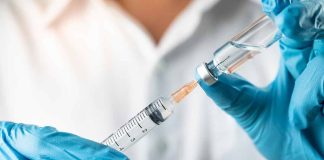 Gloved hands preparing syringe with vaccine vial.