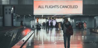 Airport sign: "All Flights Canceled", passengers walking.