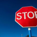 Red stop sign against a clear blue sky.