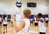 Players about to serve a volleyball in gym.