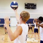 Players about to serve a volleyball in gym.