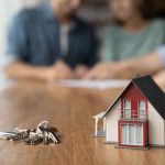 Model house and keys with couple signing documents.