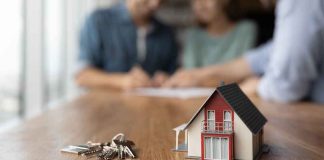 Model house and keys with couple signing documents.