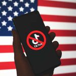 Hand holding phone with banned TikTok symbol USA flag